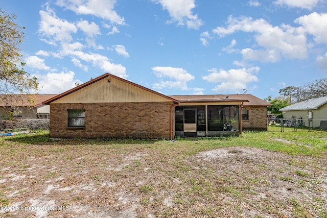 back of property featuring a sunroom, fence, a lawn, and brick siding