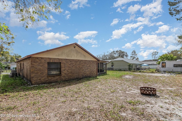 view of side of property with an outdoor fire pit, brick siding, and fence