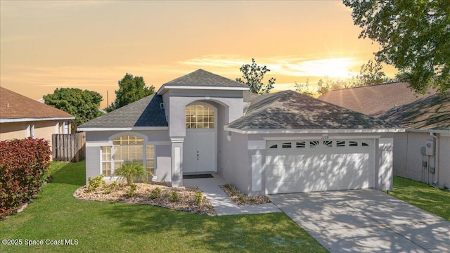 traditional home featuring stucco siding, a lawn, concrete driveway, a shingled roof, and a garage