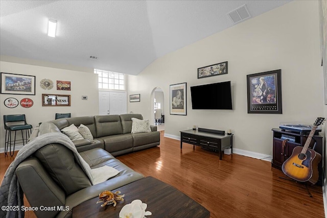 living area with visible vents, baseboards, vaulted ceiling, wood finished floors, and arched walkways