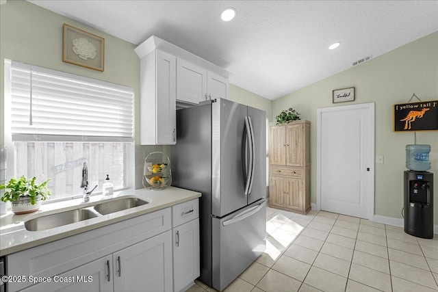 kitchen featuring visible vents, freestanding refrigerator, a sink, vaulted ceiling, and white cabinets