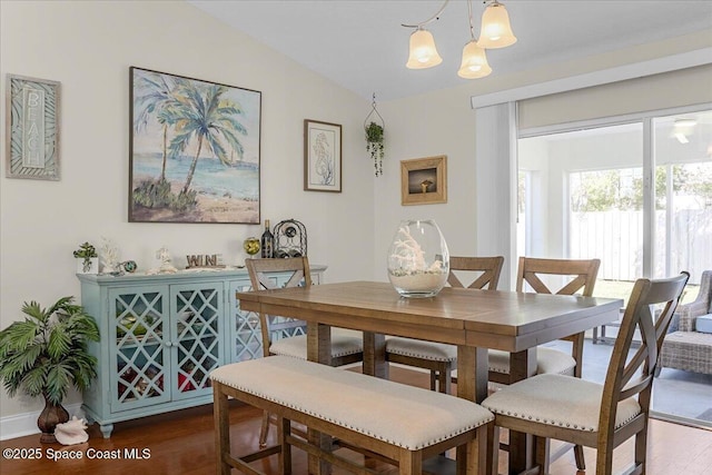 dining area with dark wood-type flooring, a chandelier, and vaulted ceiling