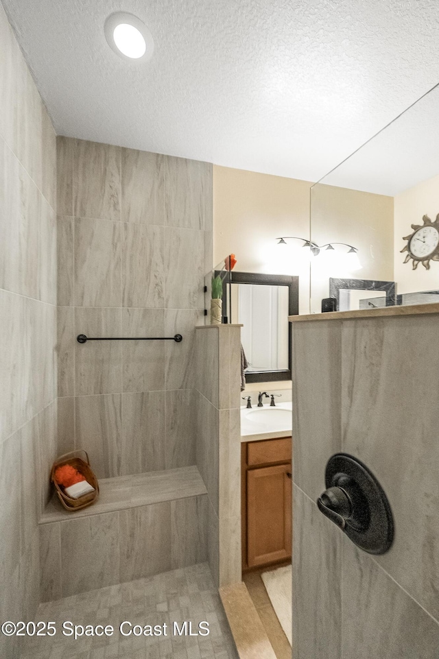 full bathroom with a tile shower, vanity, and a textured ceiling