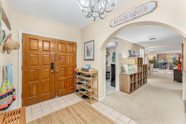 entrance foyer featuring light carpet, a textured ceiling, arched walkways, and a chandelier