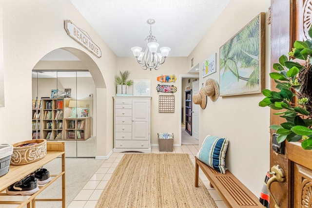 entryway featuring baseboards, arched walkways, a textured ceiling, a notable chandelier, and light tile patterned flooring