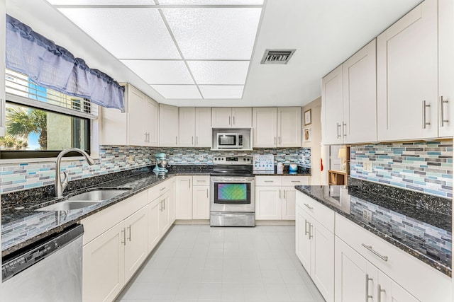 kitchen with stainless steel appliances, a sink, visible vents, decorative backsplash, and dark stone countertops