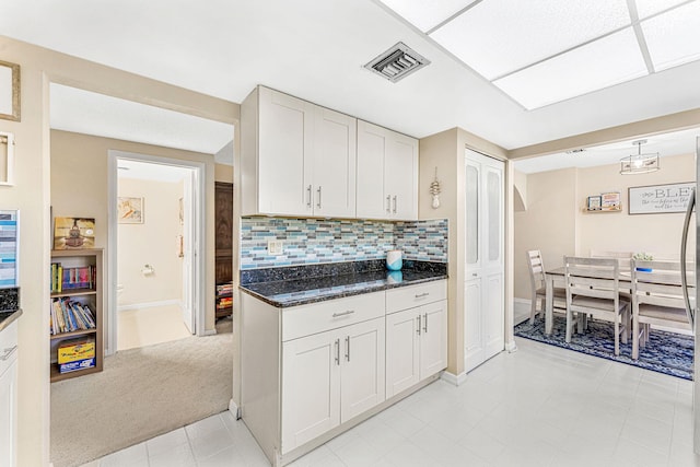 kitchen with dark stone counters, backsplash, visible vents, and white cabinetry