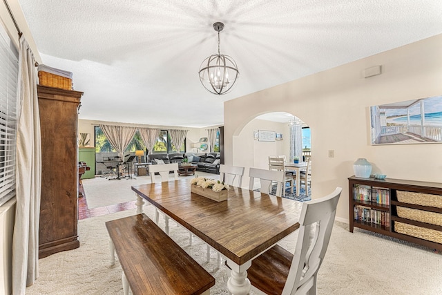 dining area featuring a textured ceiling, arched walkways, light carpet, baseboards, and an inviting chandelier