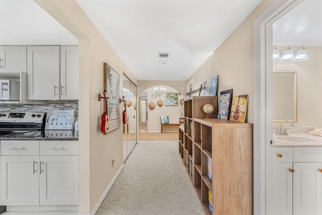 corridor featuring arched walkways, a textured ceiling, light carpet, a sink, and visible vents