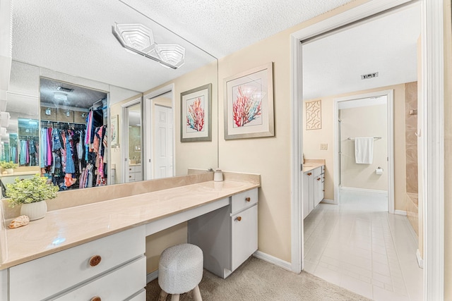 full bathroom featuring baseboards, visible vents, a walk in closet, a textured ceiling, and vanity