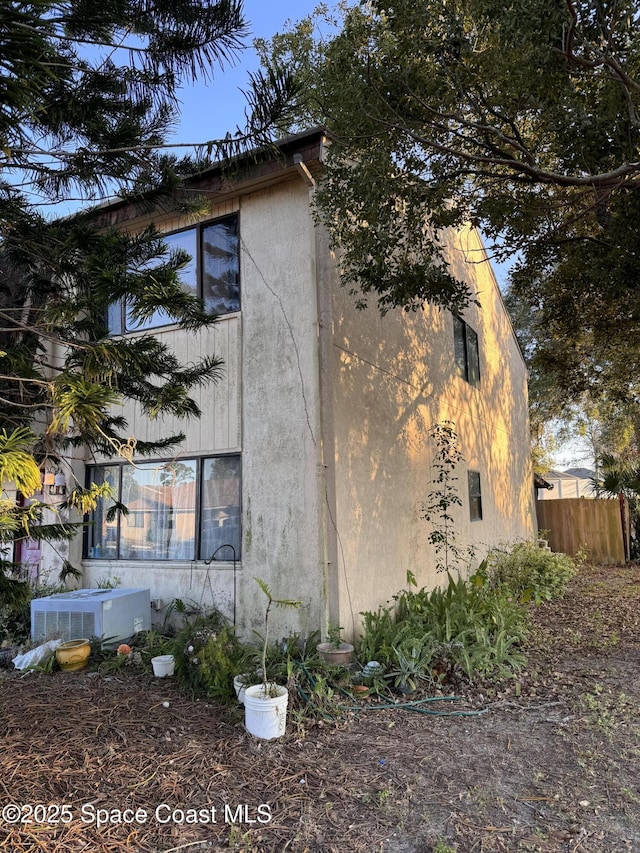 view of side of home featuring central AC unit, fence, and stucco siding