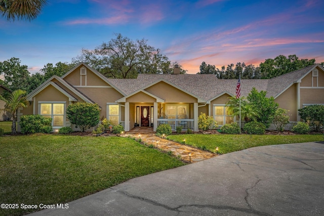 view of front of home featuring a yard, roof with shingles, stucco siding, and covered porch