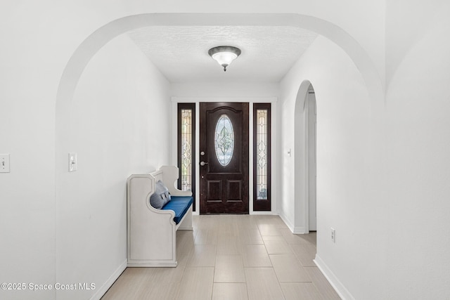 entrance foyer with arched walkways, baseboards, and a textured ceiling