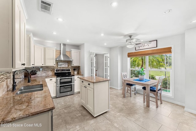 kitchen with tasteful backsplash, visible vents, a sink, wall chimney range hood, and double oven range