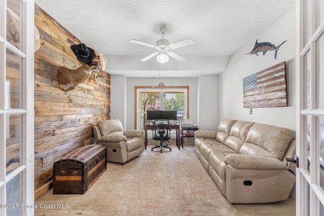 carpeted living room with wooden walls, a textured ceiling, and a ceiling fan