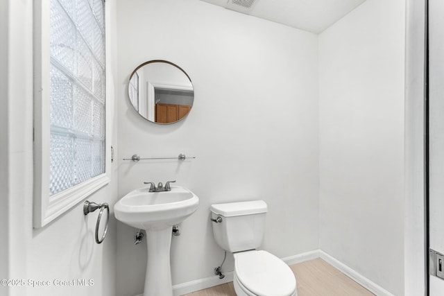 half bath with toilet, a healthy amount of sunlight, baseboards, and visible vents