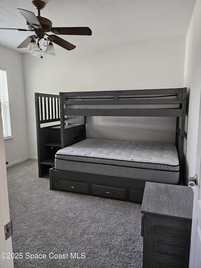 bedroom featuring baseboards, a textured ceiling, dark carpet, and a ceiling fan