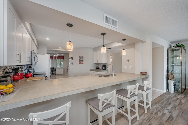 kitchen featuring visible vents, white cabinets, stainless steel microwave, a peninsula, and a sink