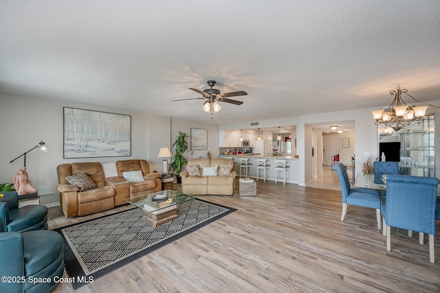 living room featuring a textured ceiling, ceiling fan with notable chandelier, light wood-style flooring, and baseboards