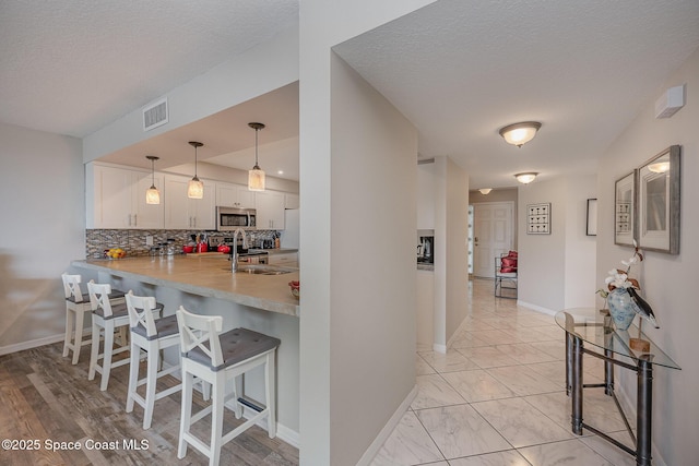 kitchen featuring a breakfast bar area, a sink, visible vents, white cabinets, and stainless steel microwave