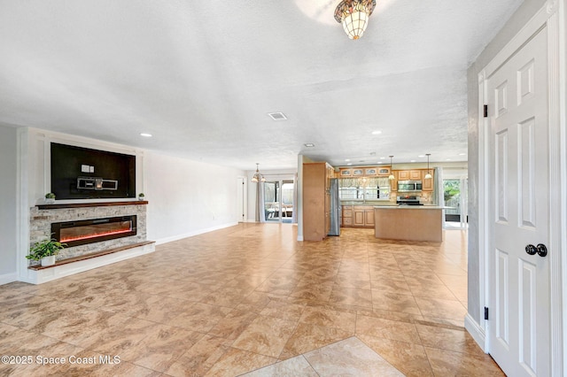 unfurnished living room featuring baseboards, visible vents, a glass covered fireplace, a textured ceiling, and recessed lighting