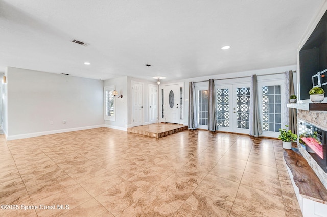 unfurnished living room featuring baseboards, visible vents, a glass covered fireplace, french doors, and recessed lighting