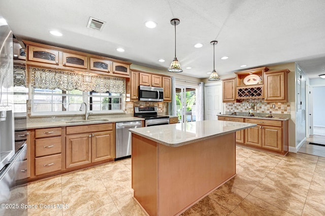 kitchen with visible vents, a kitchen island, glass insert cabinets, stainless steel appliances, and a sink