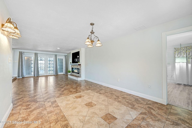 unfurnished living room featuring a glass covered fireplace, french doors, a notable chandelier, and baseboards