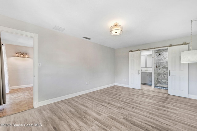 unfurnished bedroom with light wood finished floors, a barn door, and baseboards