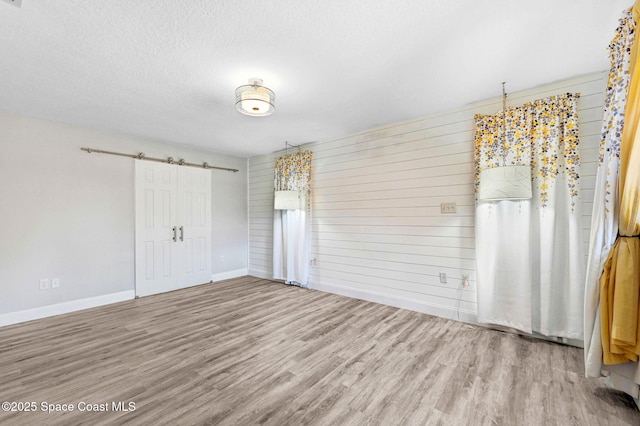 unfurnished bedroom with a closet, a barn door, a textured ceiling, wood finished floors, and baseboards