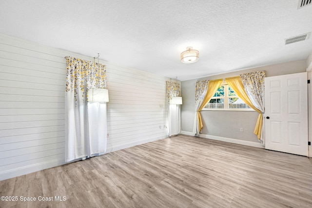 empty room with visible vents, wood walls, a textured ceiling, and wood finished floors