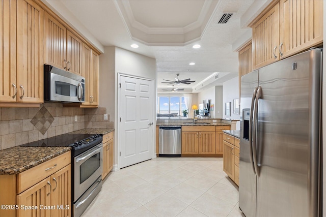 kitchen featuring dark stone countertops, a tray ceiling, a peninsula, ornamental molding, and stainless steel appliances