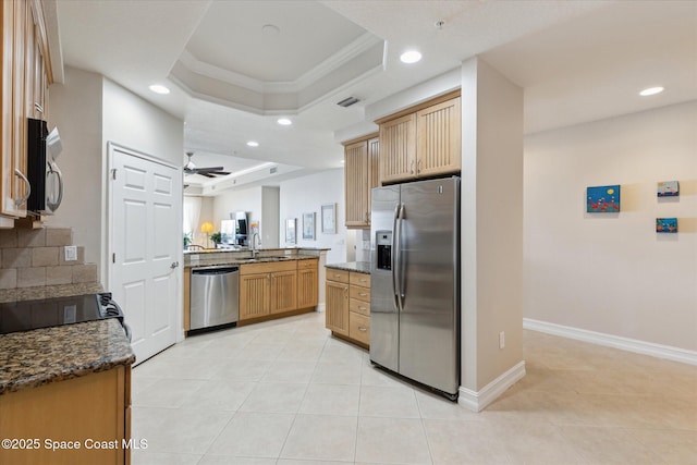 kitchen featuring a ceiling fan, a sink, a tray ceiling, appliances with stainless steel finishes, and a peninsula