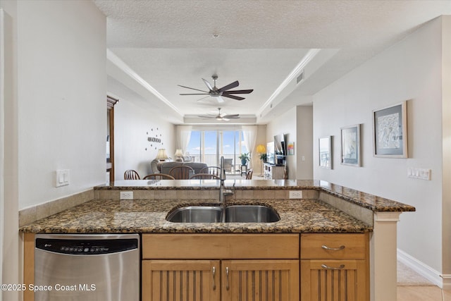 kitchen featuring dishwasher, a tray ceiling, dark stone countertops, and a sink