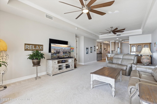 living room with a ceiling fan, visible vents, baseboards, a raised ceiling, and light colored carpet