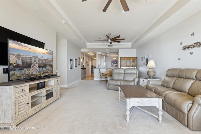 living area featuring a tray ceiling, baseboards, light colored carpet, and a ceiling fan