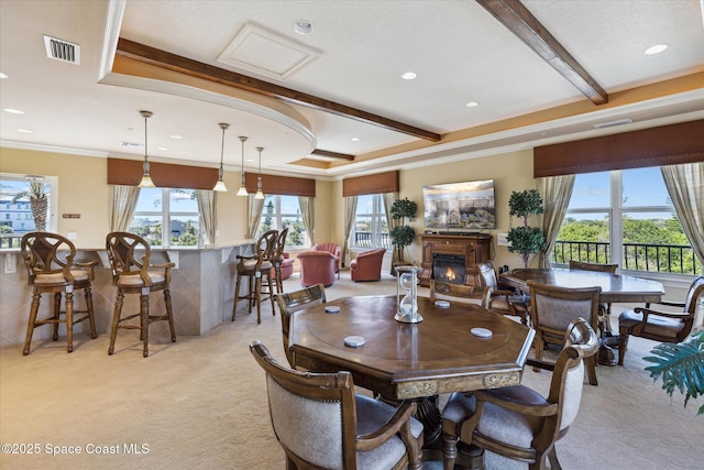 dining room featuring visible vents, beam ceiling, a glass covered fireplace, crown molding, and light colored carpet