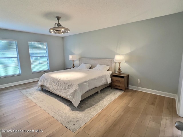 bedroom with light wood-type flooring, a textured ceiling, and baseboards