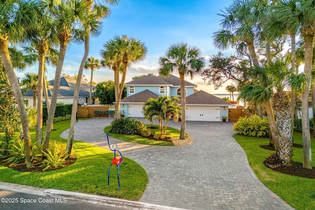 view of front of property with stucco siding, a front lawn, decorative driveway, fence, and an attached garage