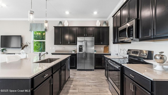 kitchen featuring stainless steel appliances, a sink, hanging light fixtures, a center island with sink, and crown molding