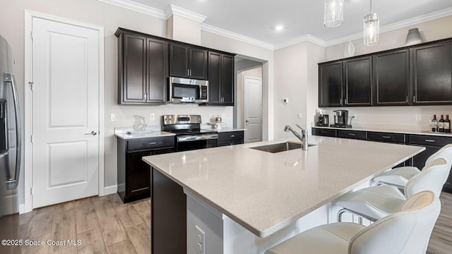 kitchen with stainless steel appliances, hanging light fixtures, a sink, and a center island with sink