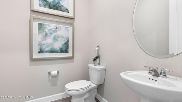 bathroom featuring toilet, baseboards, and a sink