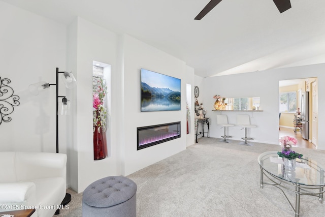 living room with ceiling fan, carpet, vaulted ceiling, and a glass covered fireplace