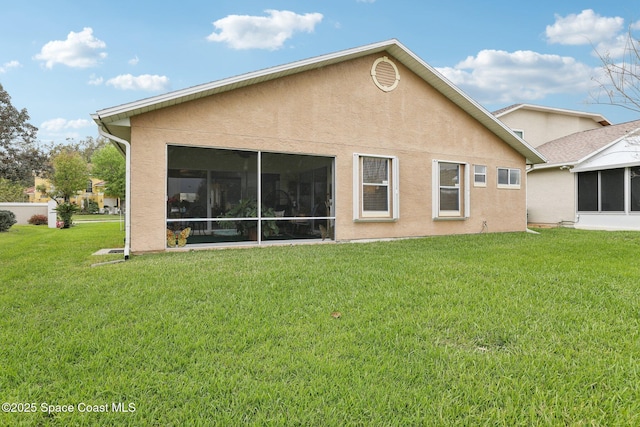 rear view of house featuring a sunroom, a yard, and stucco siding