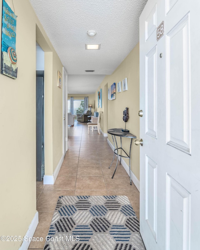 hall featuring a textured ceiling, light tile patterned flooring, and baseboards