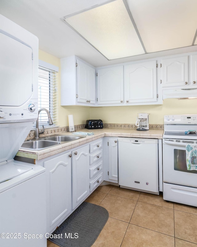 kitchen with light tile patterned flooring, under cabinet range hood, white appliances, white cabinets, and stacked washing maching and dryer