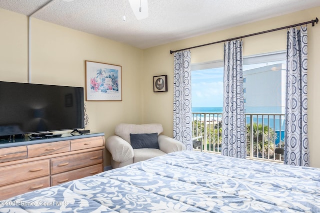 bedroom with a water view, access to exterior, and a textured ceiling