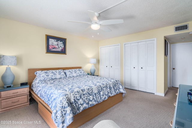 bedroom featuring light carpet, visible vents, a ceiling fan, a textured ceiling, and two closets