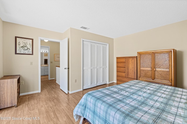 bedroom with a closet, visible vents, a textured ceiling, light wood-type flooring, and baseboards