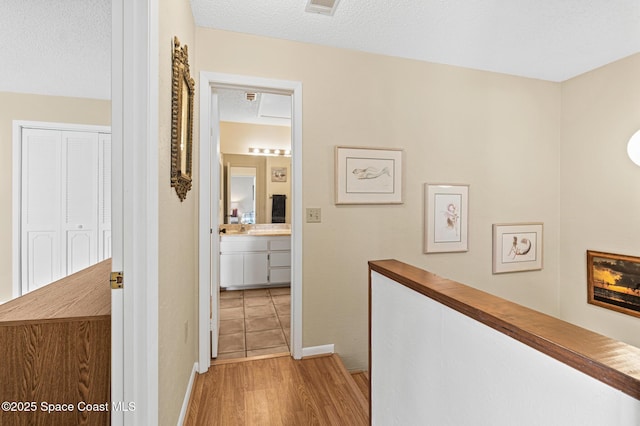 hallway featuring baseboards, a textured ceiling, and light wood finished floors